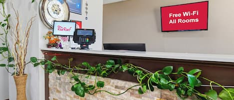 Zona de recepción con un reloj, un letrero de Red Roof, un letrero de Red Bull, un letrero de RedEye y un televisor mostrando 'Wi-Fi gratis en todas las habitaciones'.