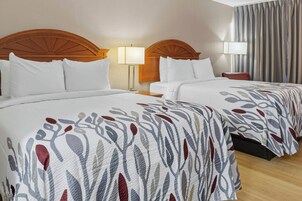 Habitación de hotel con dos camas, cabeceros de madera, ropa de cama blanca y un ventanal con cortinas.