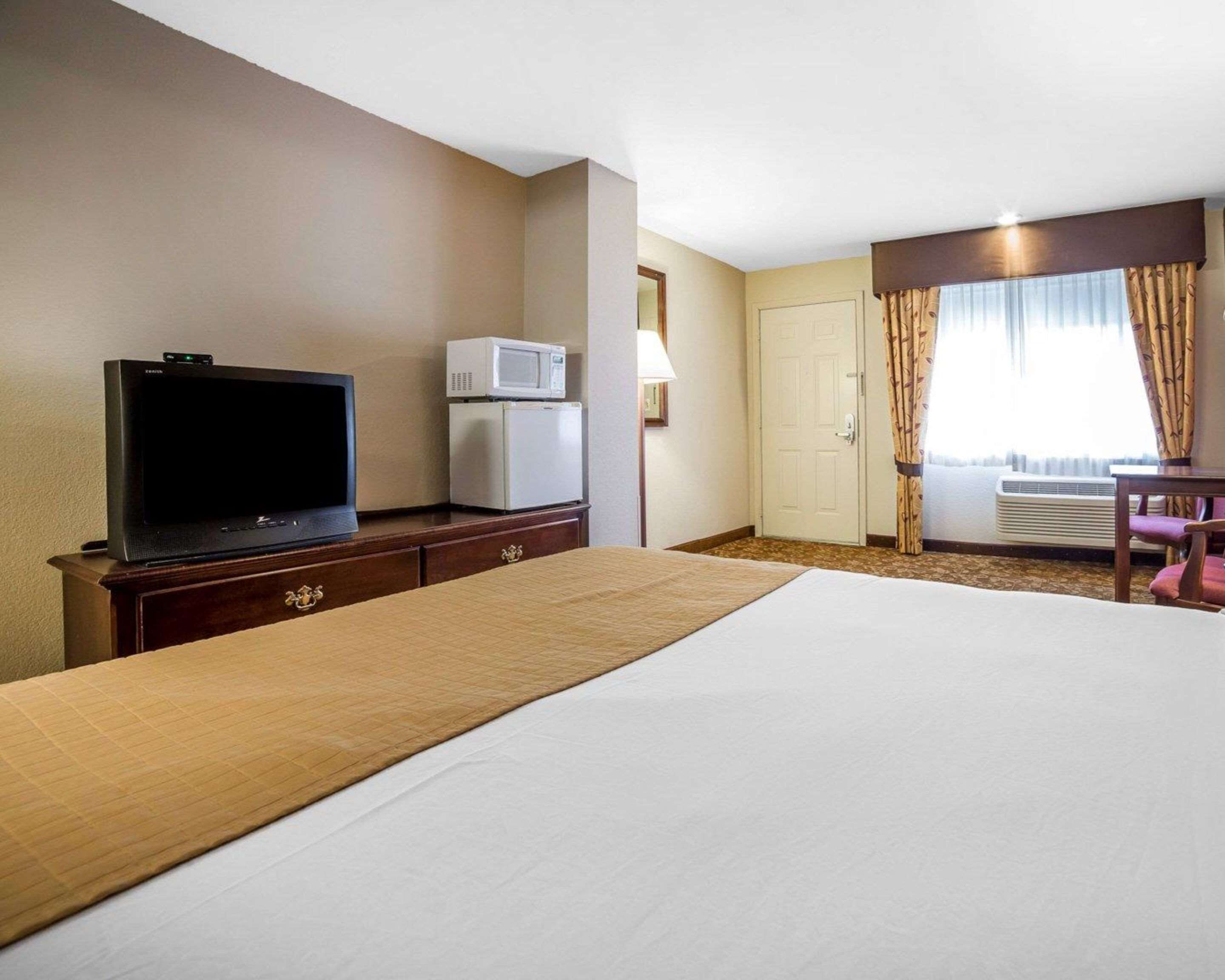 Una habitación de hotel con cama, televisión, microondas, escritorio y silla.