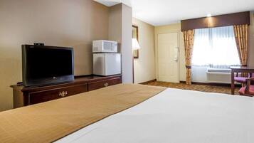Una habitación de hotel con cama, televisión, microondas, escritorio y silla.