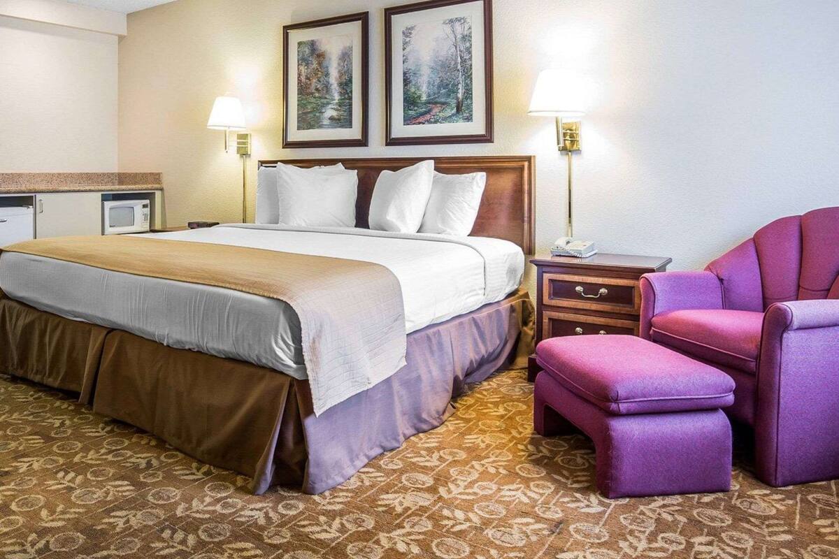 Una habitación de hotel con cama, mesita de noche, una silla y dos lámparas fijadas a la pared.