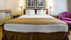 Habitació d'hotel amb un llit gran, dues imatges emmarcades a la paret, un escriptori amb una làmpada, una cadira i un microones.