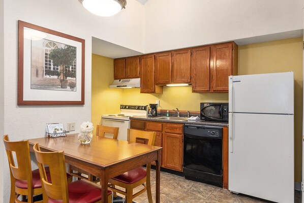 A compact kitchen with wooden cabinets, a white refrigerator, a stove, and a microwave.