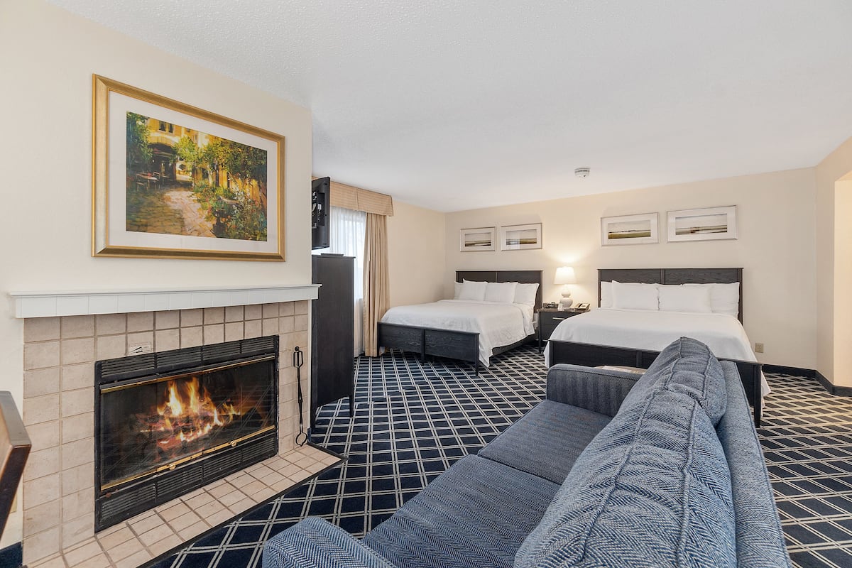 A hotel room with a fireplace, two beds, a sofa, and a painting on the wall.