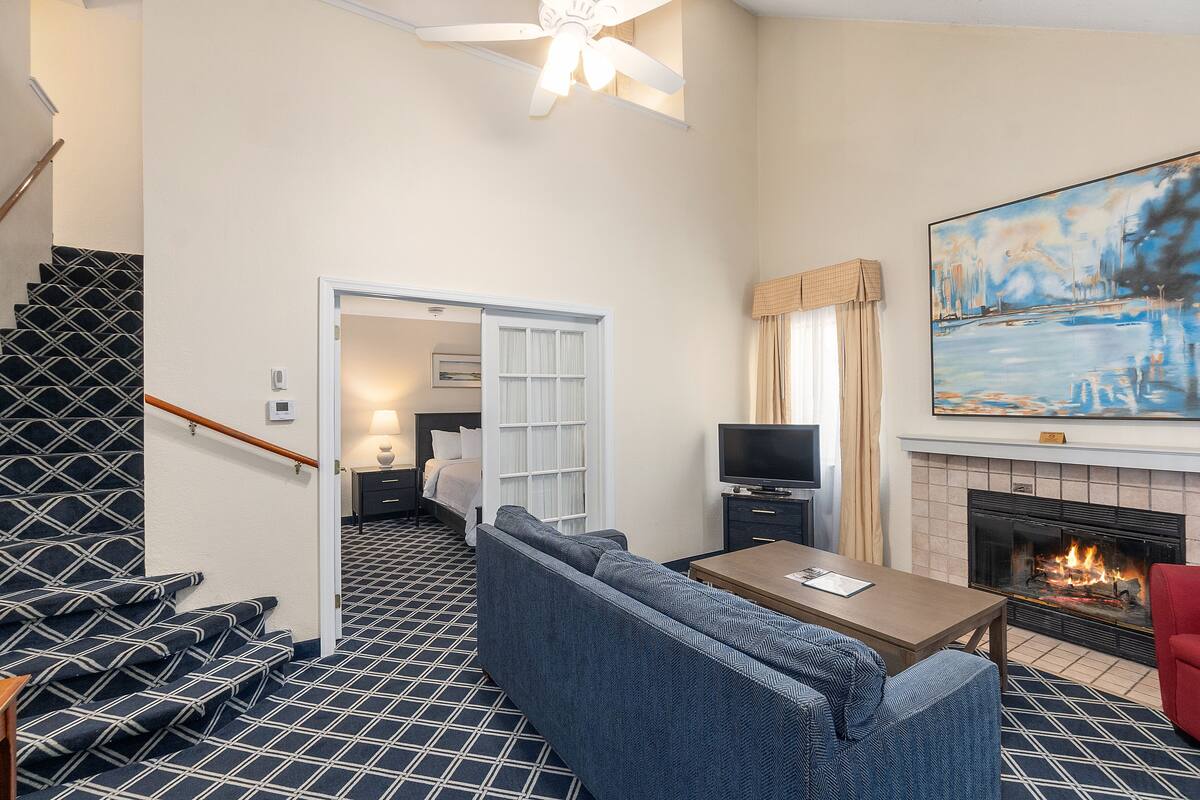 A hotel room with a patterned floor, a sofa, a red chair, a TV, a fireplace, and a painting on the wall.
