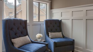 Dos sillones tapizados en azul con respaldos acolchados y detalles de costura decorativa, ubicados frente a una ventana con vista a edificios residenciales.