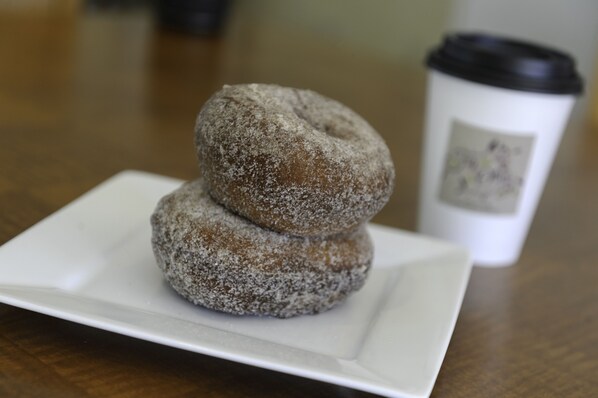 Two powdered donuts on a white plate with a coffee cup in the background.