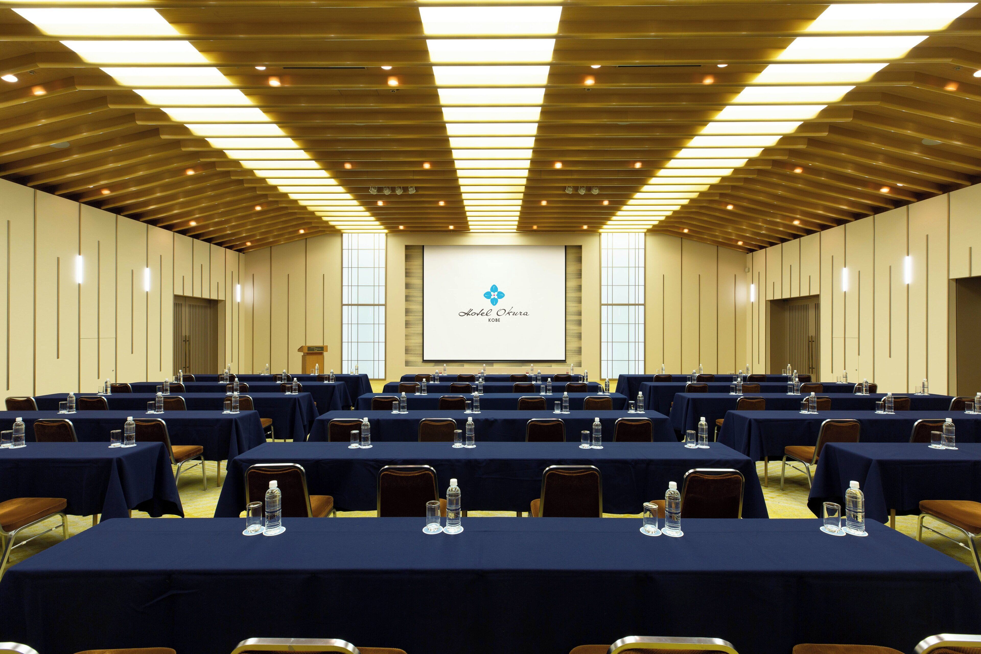 Un salón de conferencias con varias mesas, sillas y una pantalla para presentaciones.