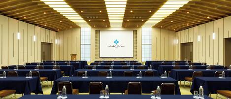 Un salón de conferencias con varias mesas, sillas y una pantalla para presentaciones.