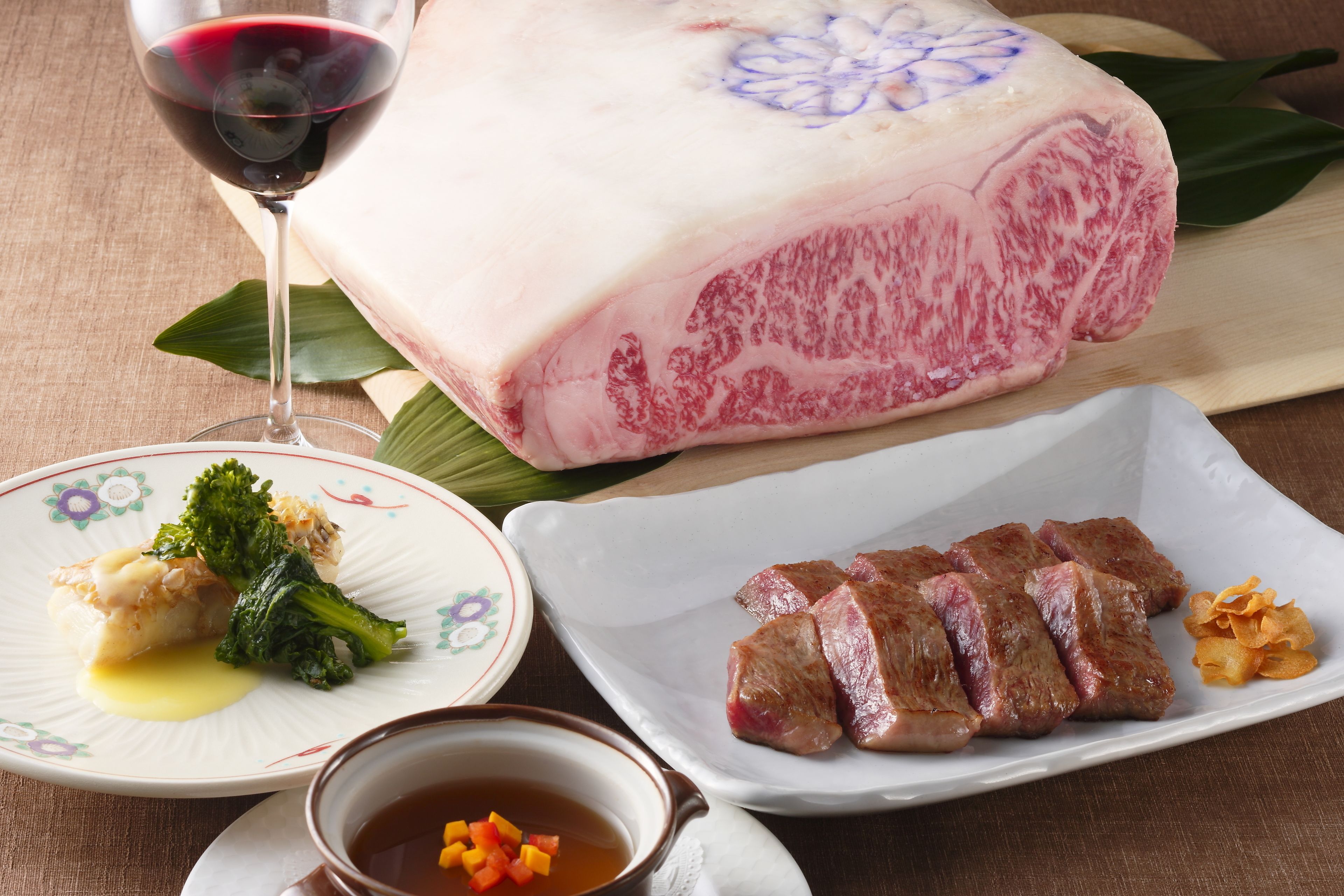 A plate with sliced meat, a glass of red wine, and a bowl of soup.