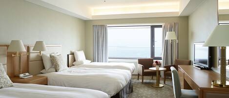 Habitación de hotel con dos camas, un escritorio, una silla, un televisor y vista al mar.