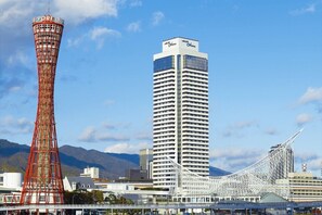 Una torre alta de color rojo con un letrero, un moderno edificio blanco con balcones, y una estructura blanca única con techo curvo.