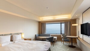 A hotel room with a large bed, a desk, a chair, a TV, and a window with a view of the sea. - Hotel Okura Kobe (Kobe)