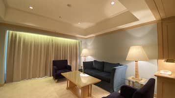 Habitación de hotel con sofá, dos sillones, una mesita, una lámpara y un escritorio con teléfono.