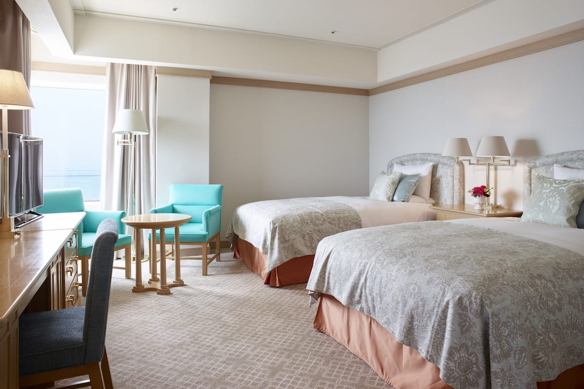 A hotel room with two beds, a desk with a chair, a small table, and a TV.