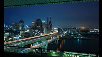 Paisagem urbana noturna com edifícios iluminados, um rio e uma ponte com rastros de luz de veículos em movimento.