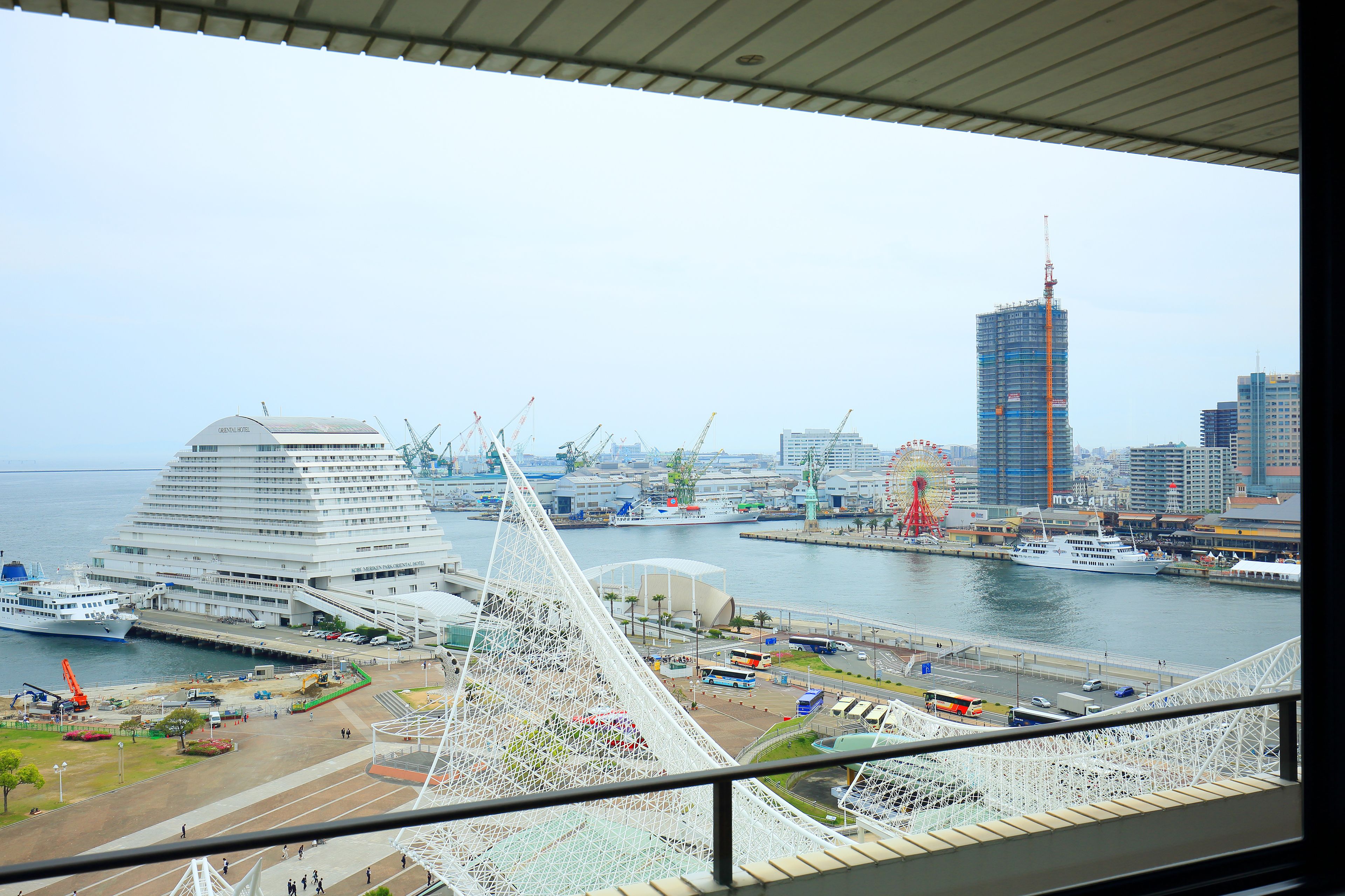A view of a cruise ship docked at a port with a large building and a Ferris wheel in the background.