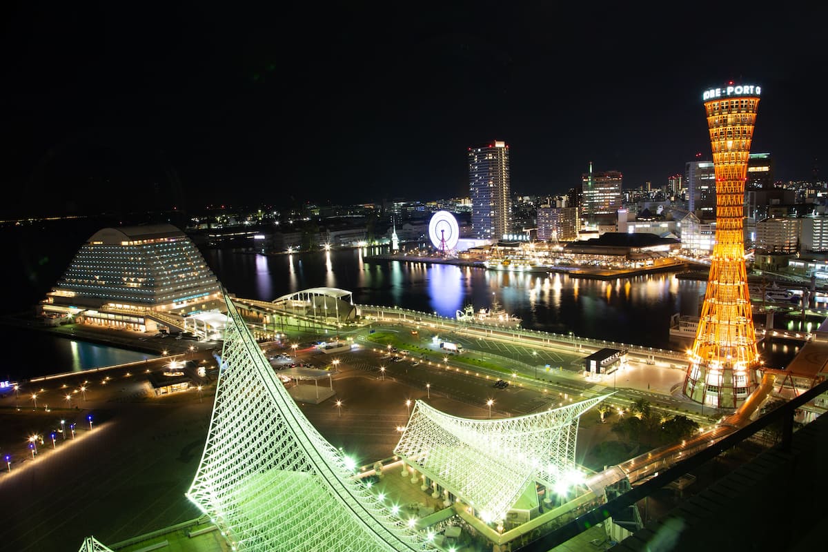 A nighttime cityscape with illuminated buildings, a prominent tower, and a large Ferris wheel.