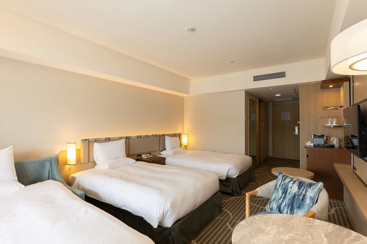 A hotel room with three beds, a desk, a chair, and a television.