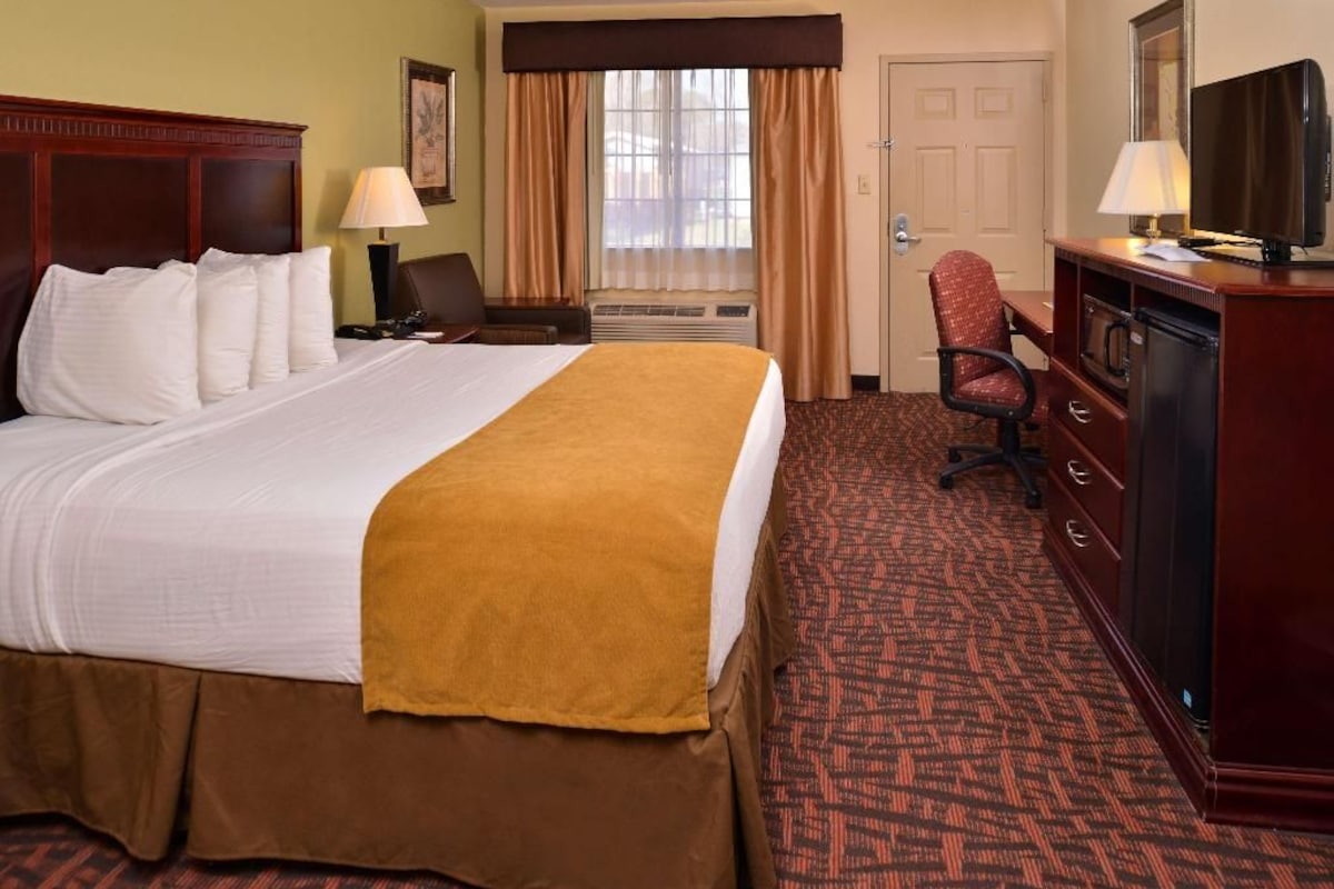 A hotel room with a large bed, a desk with a chair, a television, and a wardrobe.
