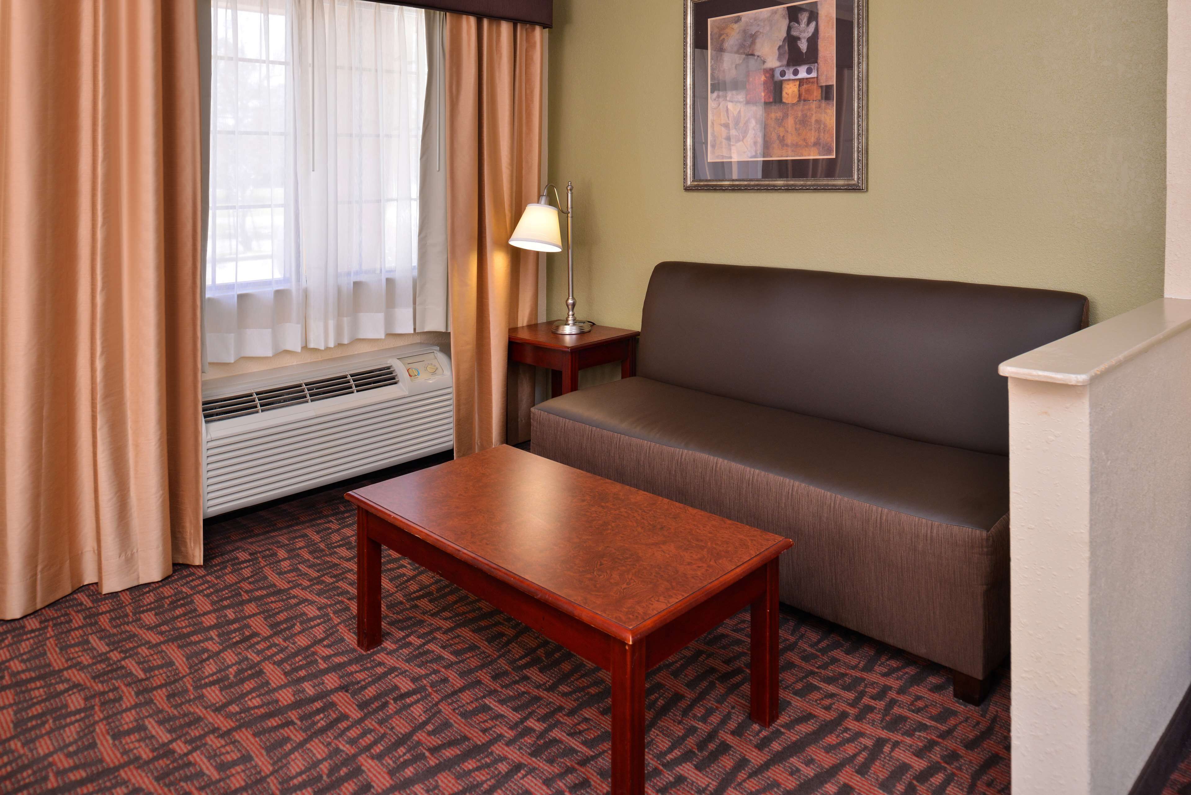 A hotel room with a brown sofa, a wooden table, a lamp, and a framed picture on the wall.