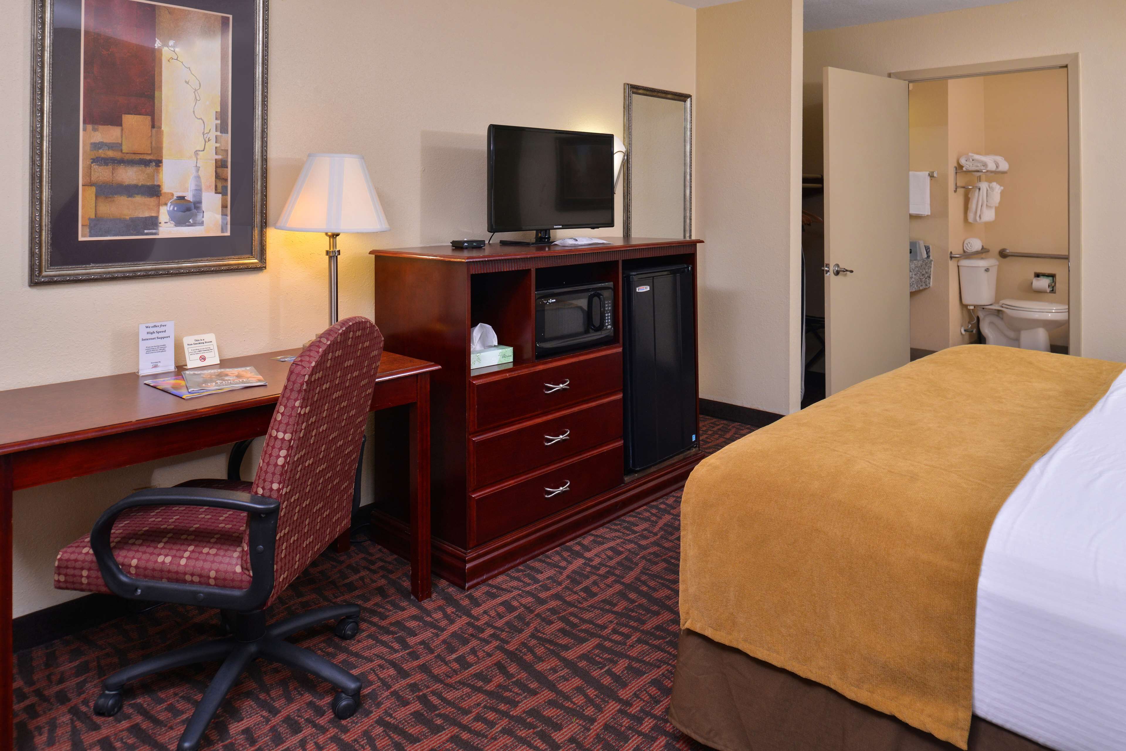 A hotel room with a desk, chair, television, microwave, and a bed with a yellow blanket.