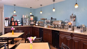 A kitchen with a granite countertop, wooden cabinets, and various appliances including a coffee maker, toaster, and blender. There is a dining table with chairs and a vase of flowers. - Best Western Eunice (Eunice)