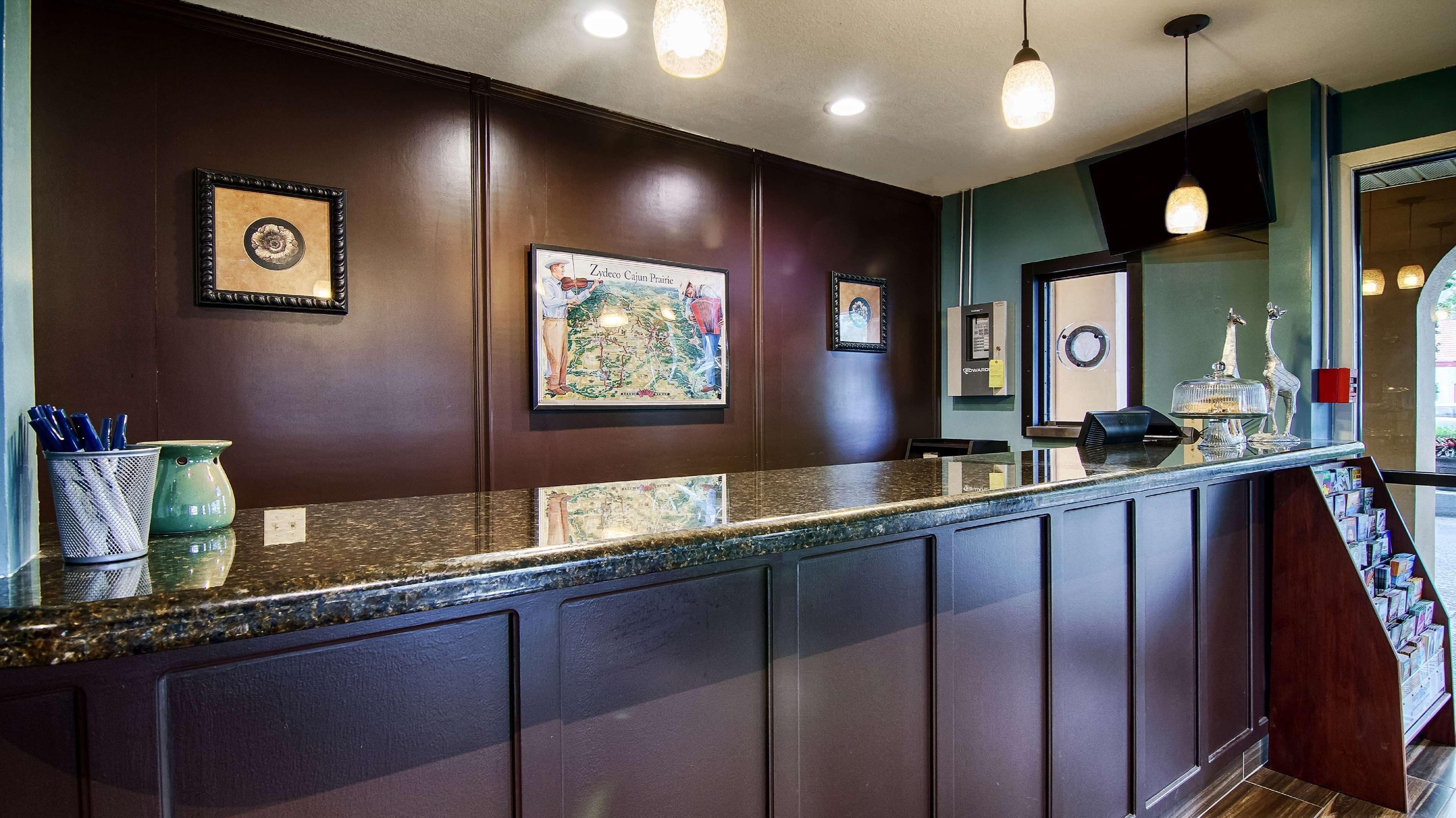 A reception area with a dark wood reception desk, framed artwork on the walls, and a view of the lobby.