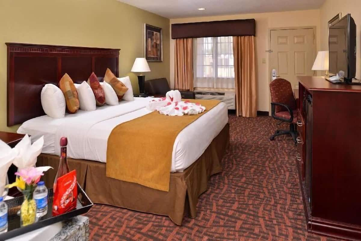 A hotel room with two beds, a desk, a chair, a television, and a window with curtains.
