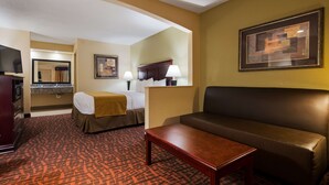 A hotel room with a bed, a sofa, a table, a TV, a mirror, and a painting on the wall. - Best Western Eunice (Eunice)