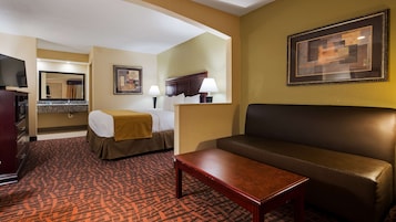 Quarto de hotel com cama, sofá, mesa, televisão, espelho e um quadro na parede.