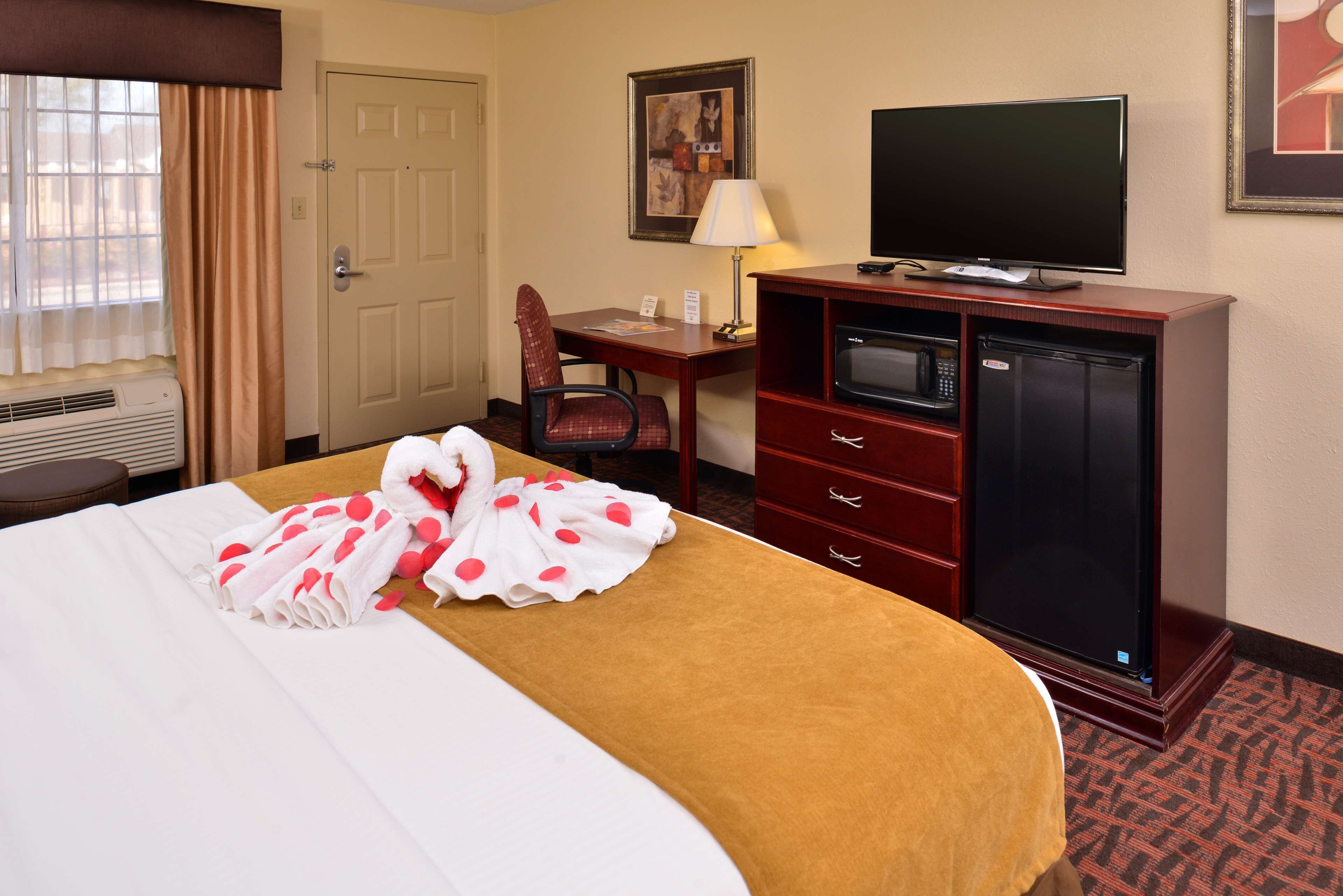 A hotel room with a bed, a desk, a television, a microwave, and a dresser.
