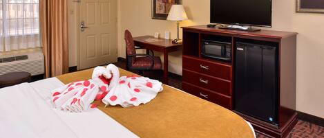 A hotel room with a bed, a desk, a television, a microwave, and a dresser.