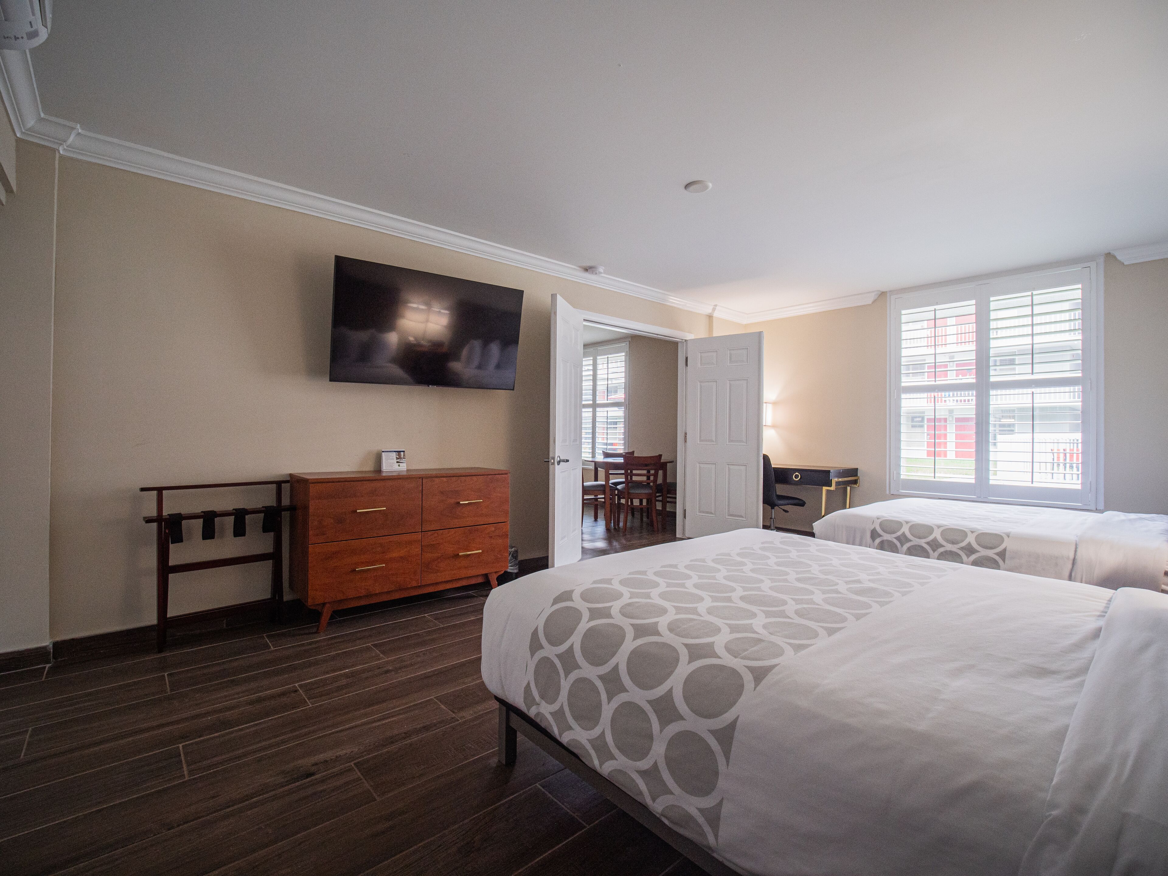 A hotel room with two beds, a wooden dresser, a television on the wall, and a window with blinds.