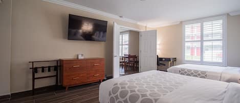 A hotel room with two beds, a wooden dresser, a television on the wall, and a window with blinds.