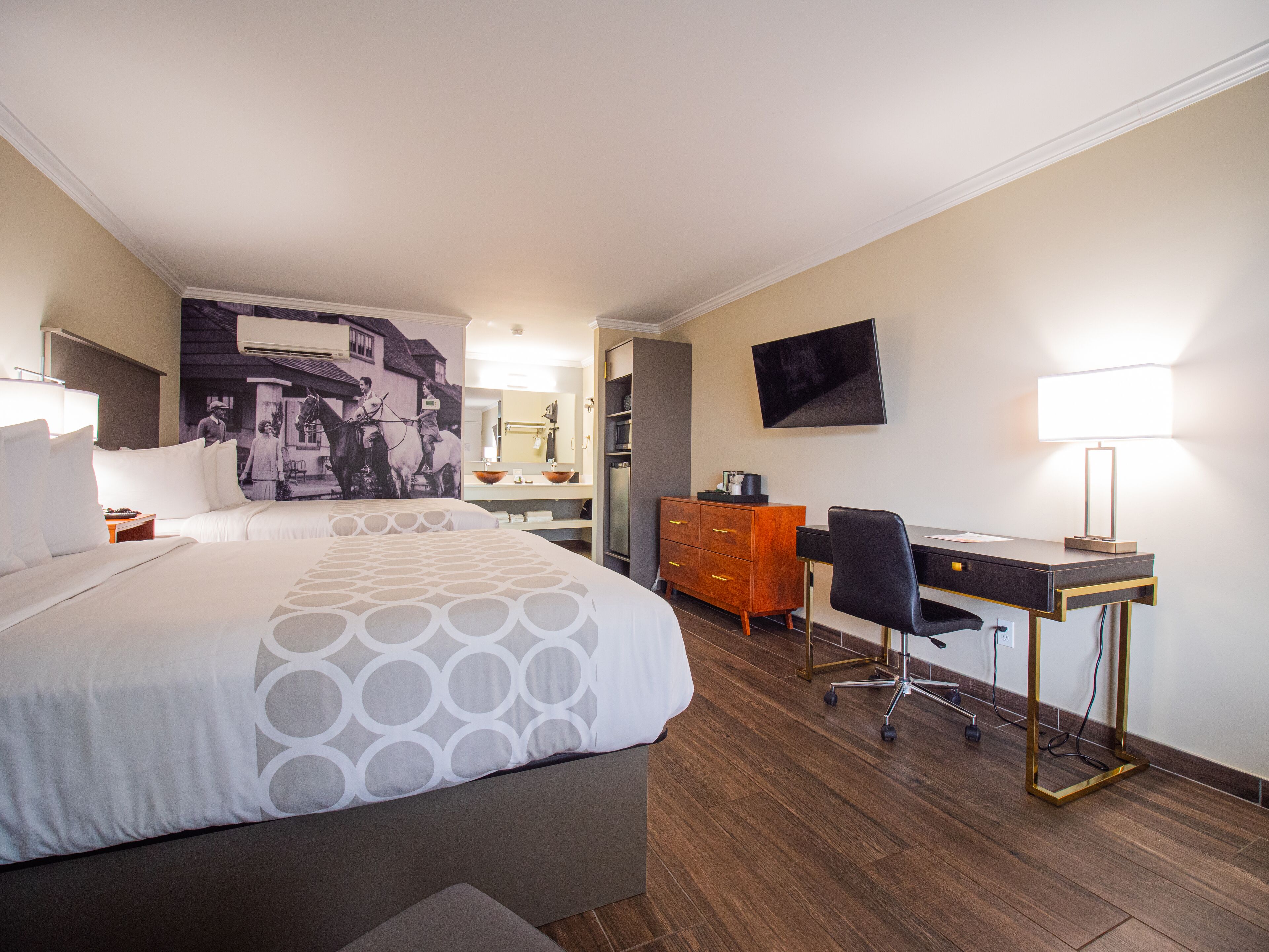 A hotel room with a large bed, a desk with a chair, a dresser, a flat-screen TV, and a bathroom visible through an open door.