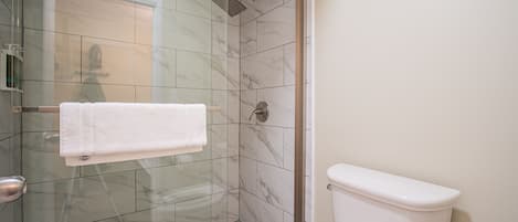 Un baño con ducha de vidrio, inodoro blanco y piso de baldosas.