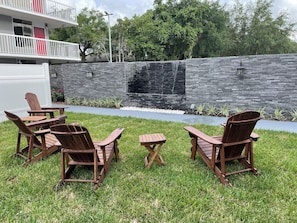 A patio with wooden chairs and tables, a stone wall, and a small waterfall feature.