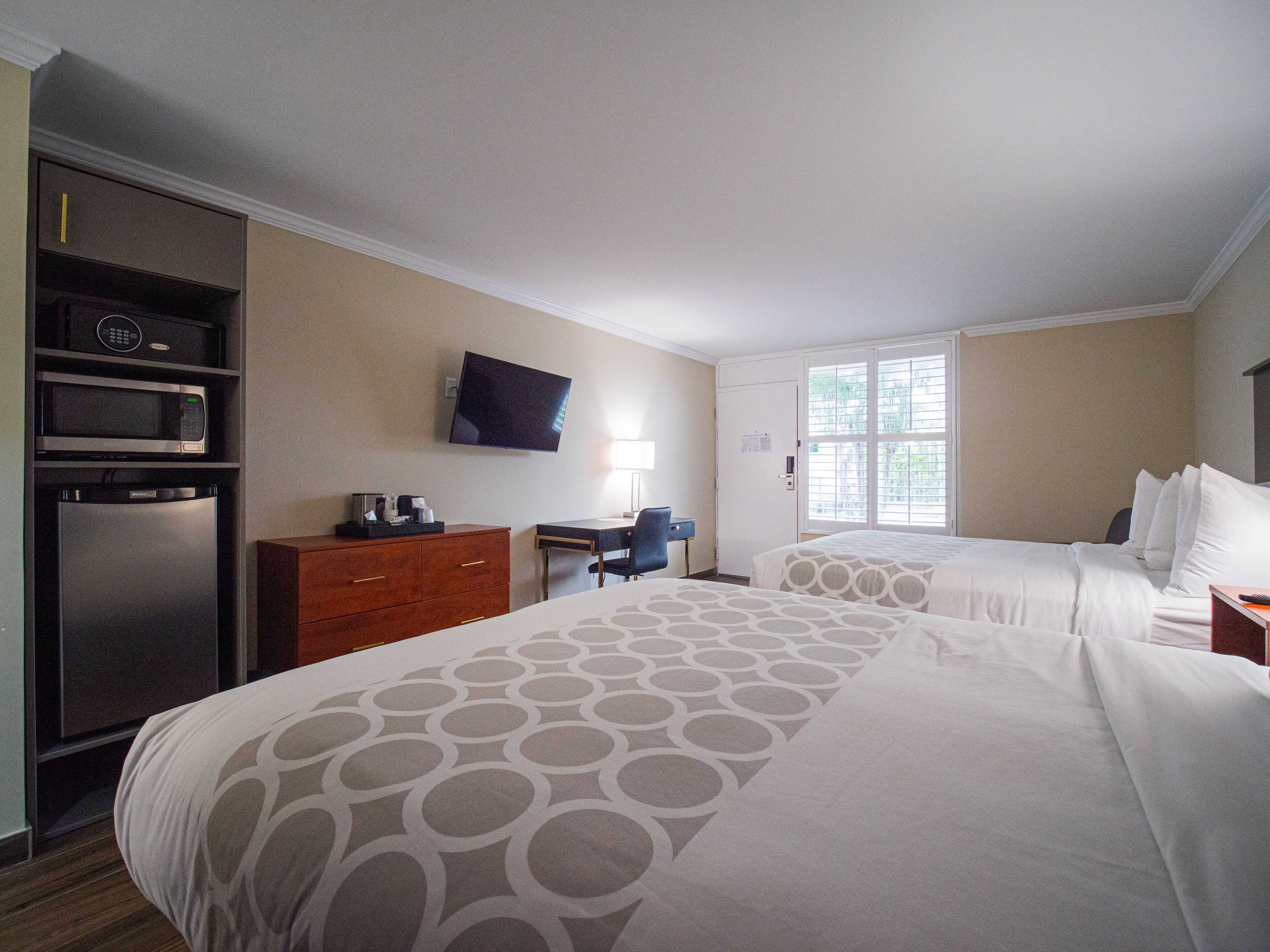 A hotel room with two beds, a desk, a chair, a TV, a microwave, and a refrigerator.