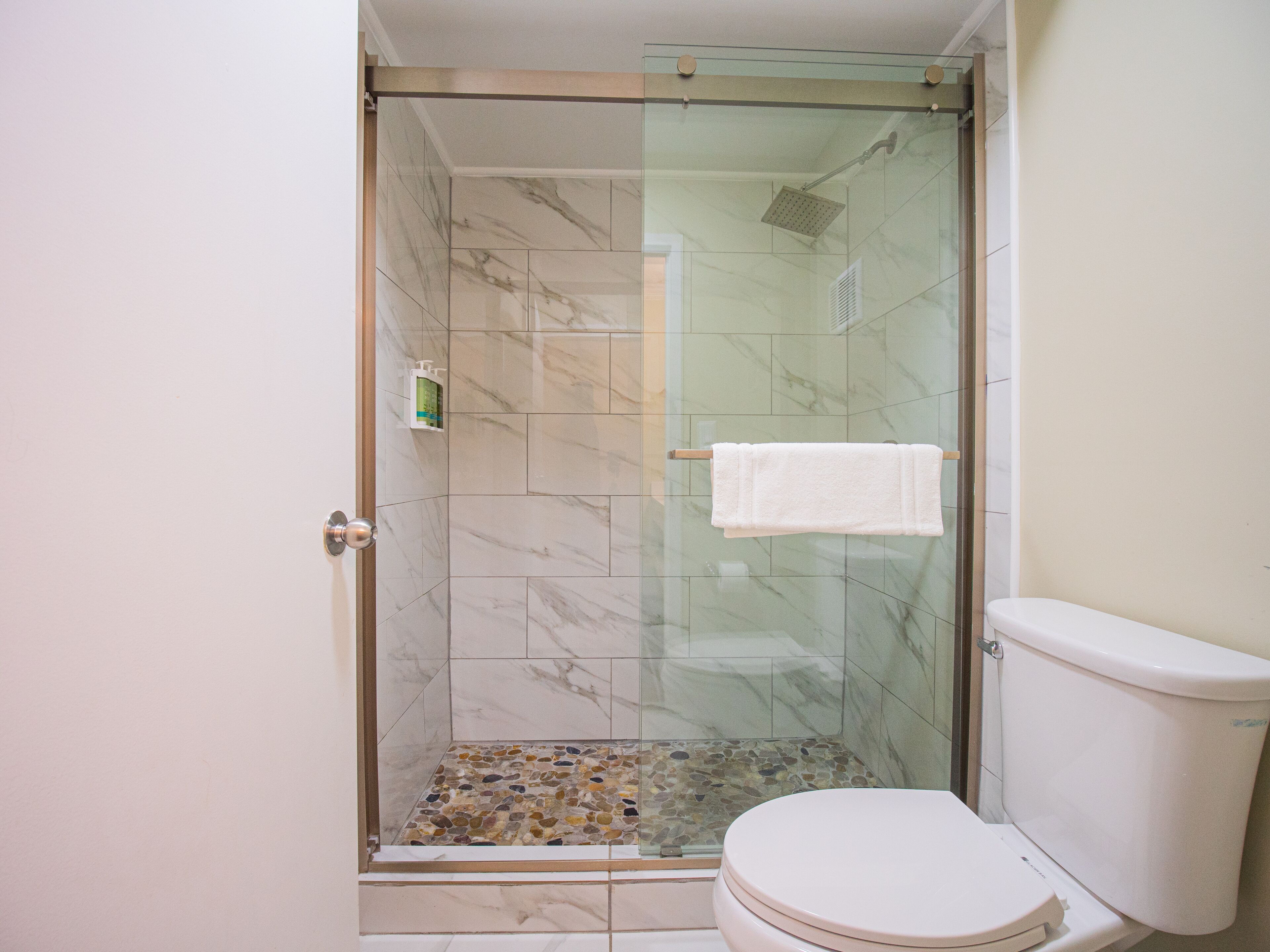 Un baño con ducha de vidrio, inodoro y suelo de mármol.