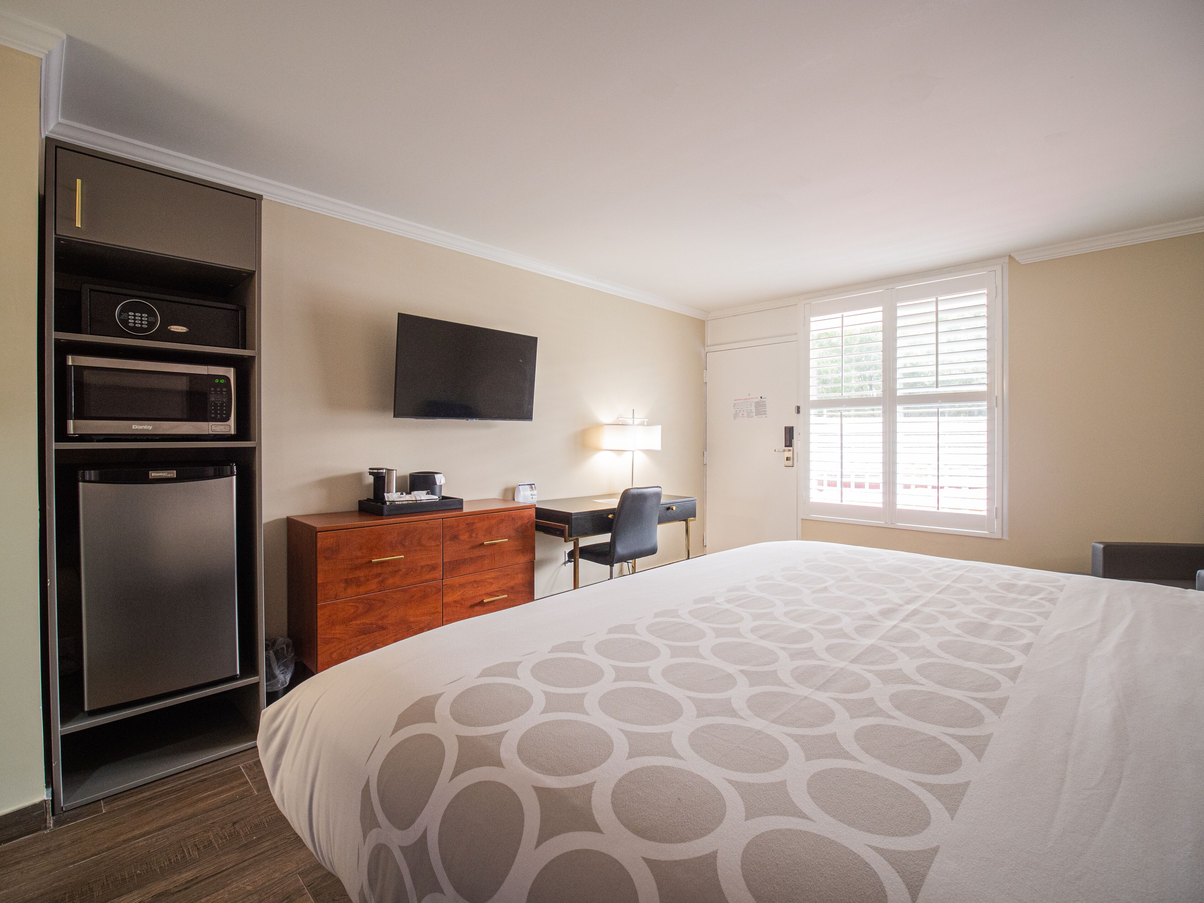 Habitación de hotel con cama, escritorio, silla, armario, microondas y televisor.