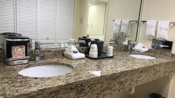 Un baño con encimera de granito, dos lavabos, una cafetera y un espejo.