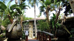Un jardin tropical avec un pont en bois menant à un bâtiment en pierre.