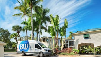 Une navette de plage arborant le logo « Best Western » est stationnée devant une maison bordée de palmiers.