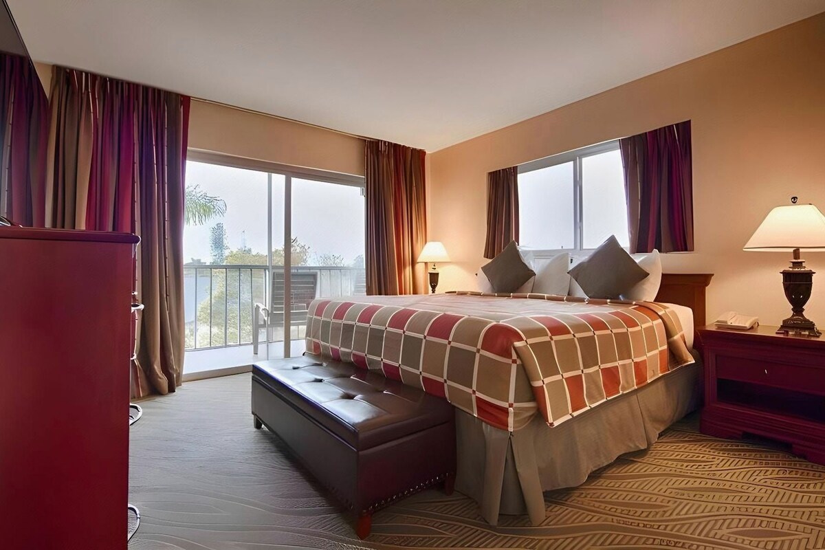 Une chambre d’hôtel avec un grand lit, un bureau, une chaise, une fenêtre et un balcon.