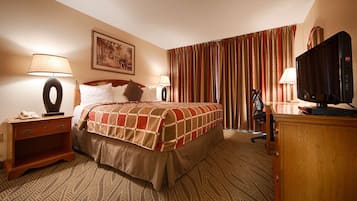 A hotel room with a bed, a desk with a lamp, a television, and a painting on the wall.