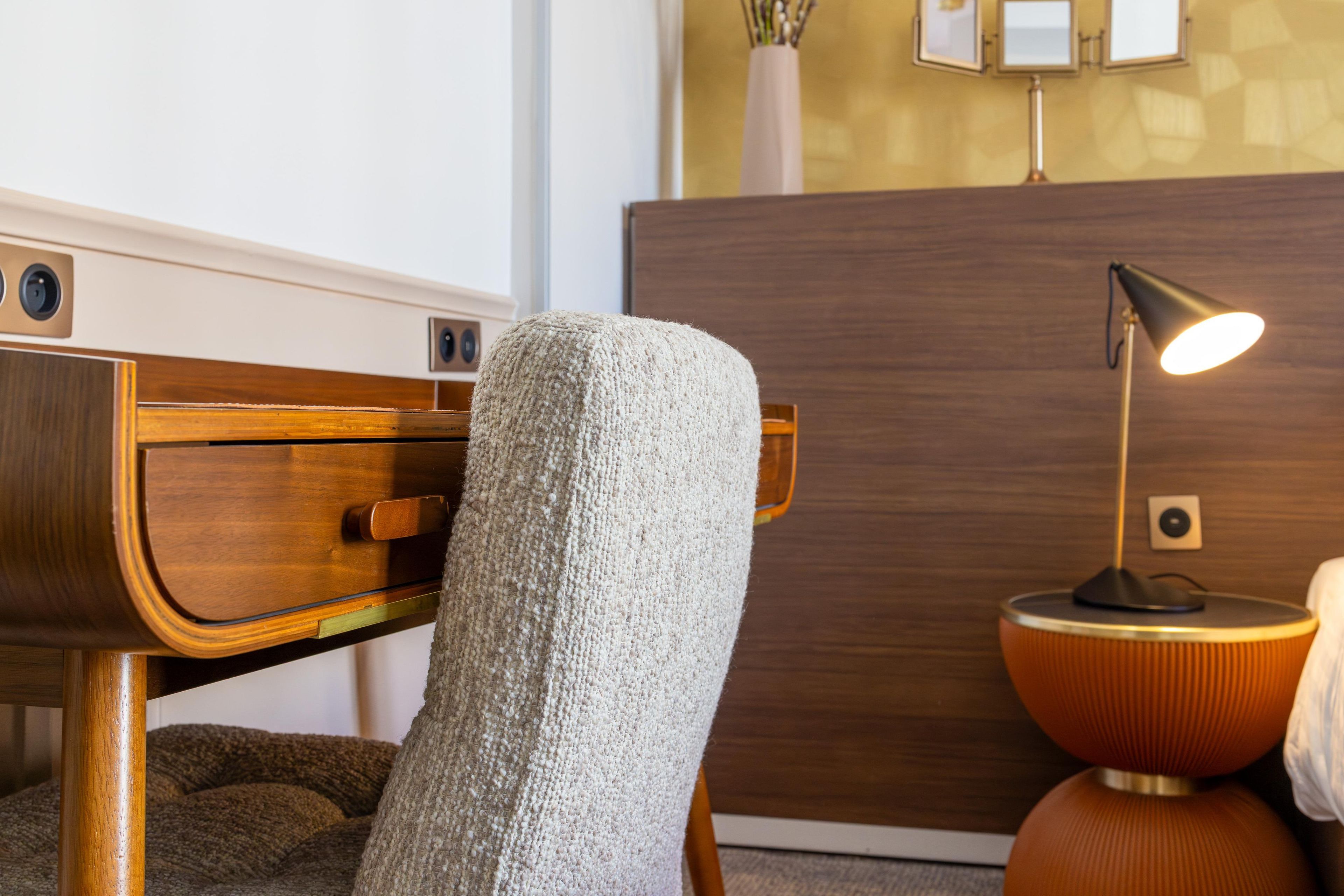 Una habitación moderna con cabecera de madera, un sillón texturizado, una mesita redonda con lámpara y un armario de madera.