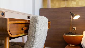 Una habitación moderna con cabecera de madera, un sillón texturizado, una mesita redonda con lámpara y un armario de madera.