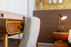 A modern room with a wooden headboard, a textured armchair, a round side table with a lamp, and a wooden cabinet.
