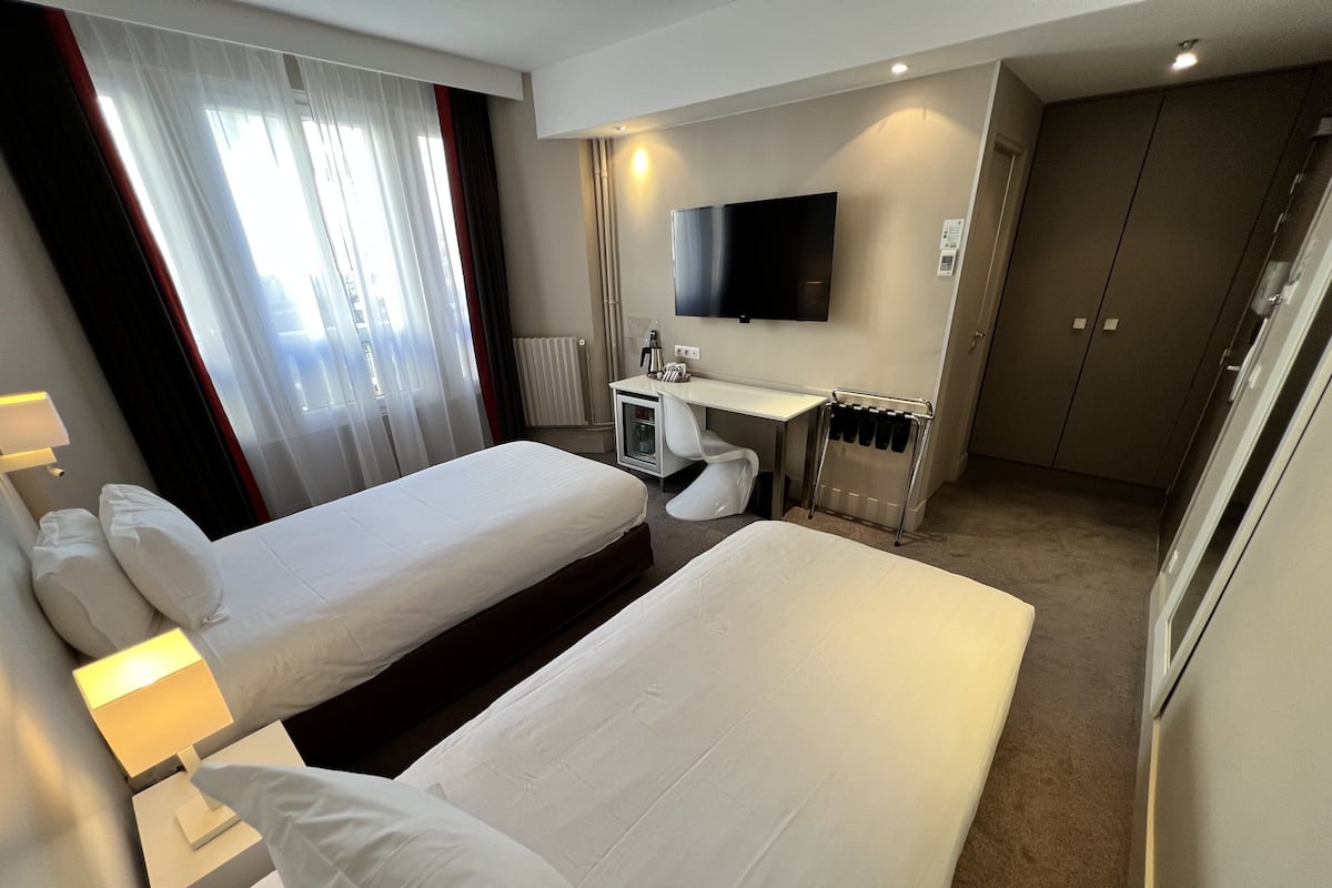 A hotel room with two beds, a desk, a TV, and a minibar.